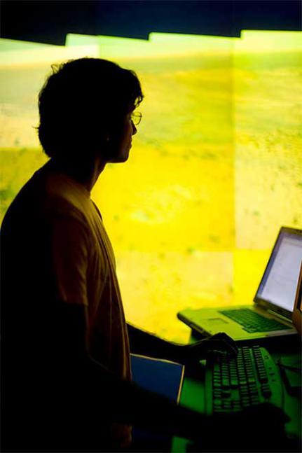 Silhouette of a young man standing at a computer keyboard and looking at a laptop